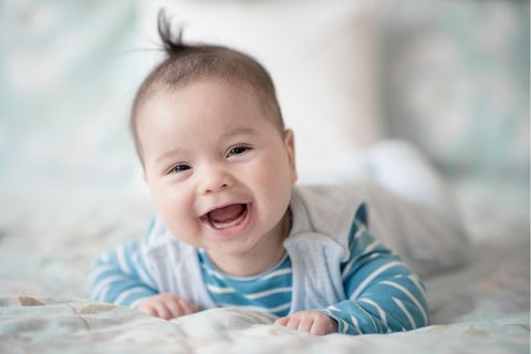 Ein Baby liegt auf einer Decke und lächelt zufrieden in die Kamera