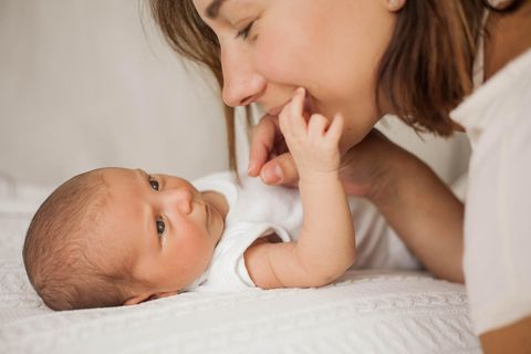 Ein Baby liegt auf dem Rücken und greift mit seiner Hand zum Mund der Mutter