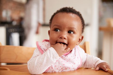 Ein Baby sitzt auf einem Hochstuhl und hat seine Hand im Mund