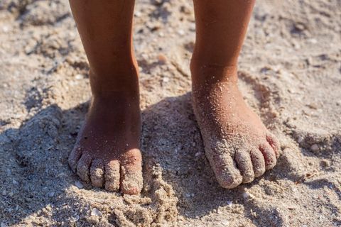 Barfuß laufen: Kinderfüße, die Barfuß im Sand stehen