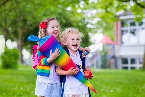Erster Schultag: Zwei Kinder stehen auf einer Wiese und halten lachend eine Schultüte in den Händen