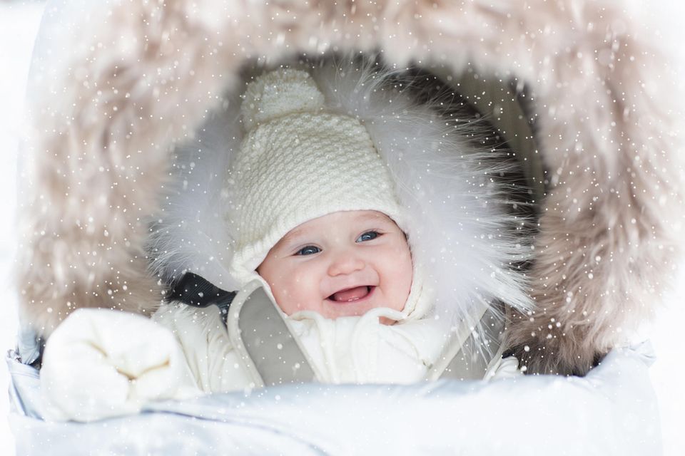 Lammfell im Kinderwagen: Fröhliches, winterlich eingepacktes Baby im fellgepolsterten Buggy.