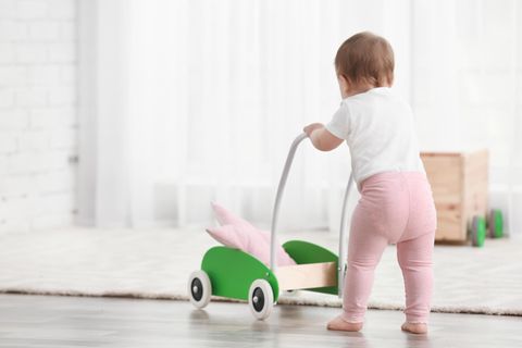 Lauflernwagen-Test: Rückenansicht eines Kleinkindes, das sich stehend an grünem Lauflernwagen festhält.