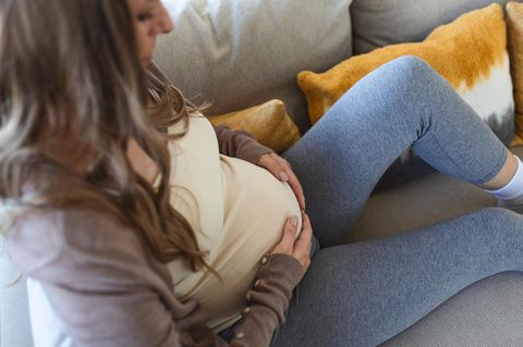 Schwangere Frau sitzt auf dem Sofa und hält ihren Bauch