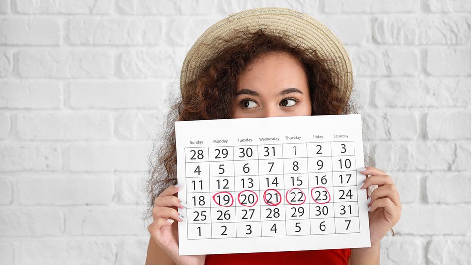 Frau hält Kalender mit markierten Tagen vor ihr Gesicht.