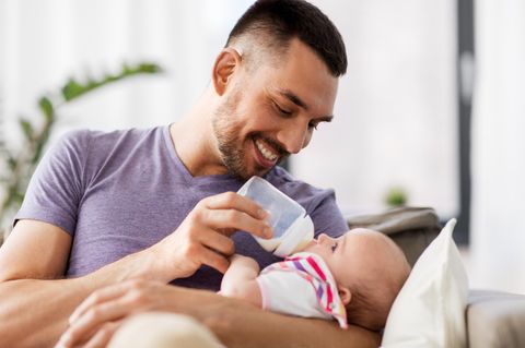 Vater füttert sein Baby lächelnd mit dem Fläschchen