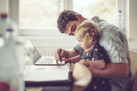 Ein Vater hat seine Tochter auf dem Schoß und arbeitet am Laptop