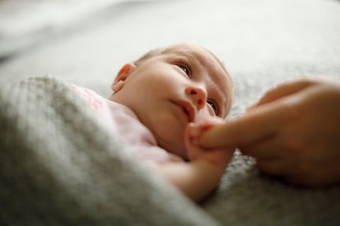 Ein Baby liegt auf einer Decke und greift nach einem Finger.