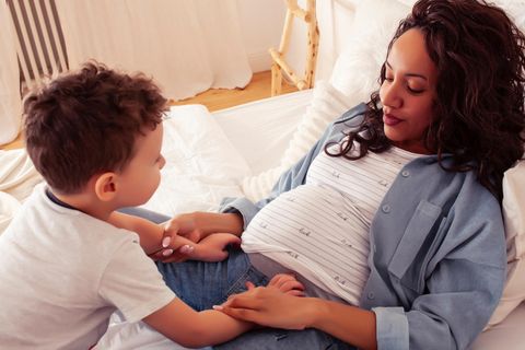 Zweite Schwangerschaft: eine schwangere Mutter liegt mit ihrem kleinen Sohn auf dem Bett