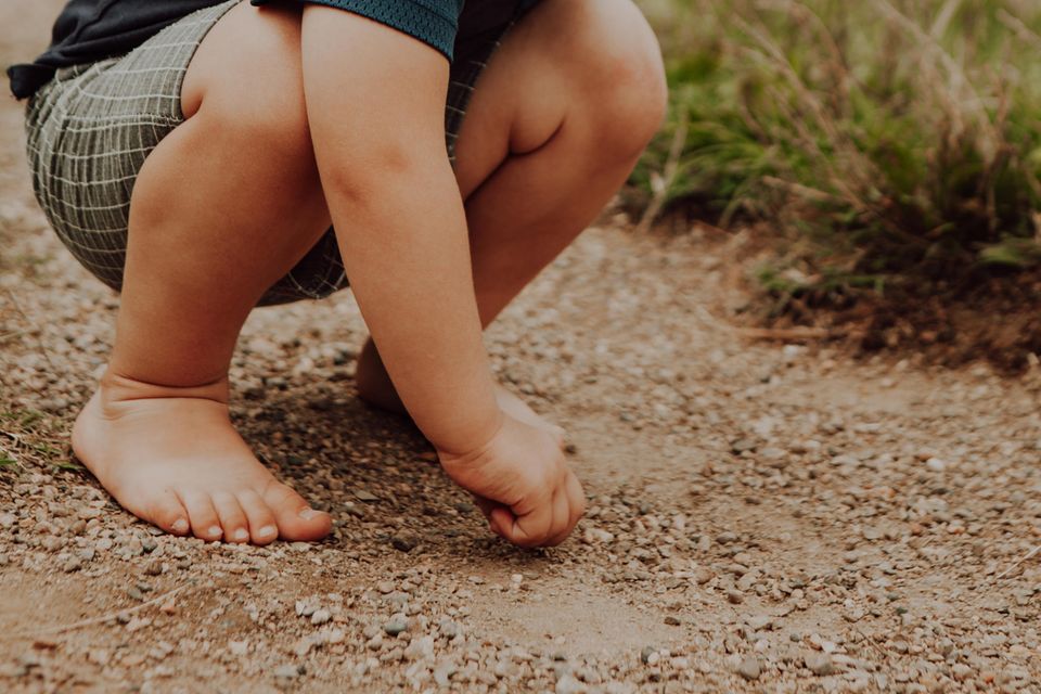 Barfußschuhe fühlen sich für Kinder wie barfuß an: Kind hockt ohne Schuhe auf Kieselsteinen.