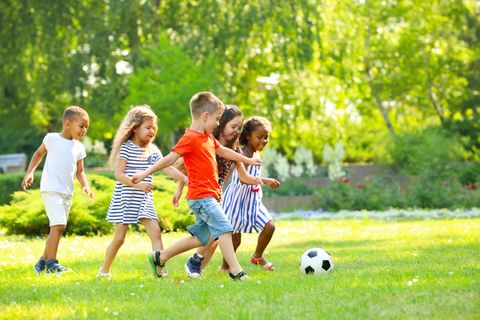 Bewegungsspiele: Eine Gruppe von Kindern läuft auf einer grünen Wiese hinter einem Fußball her