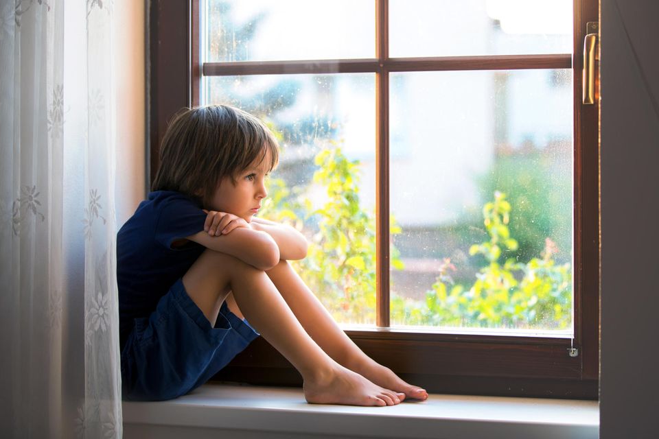 Ein Kind sitzt traurig auf der Fensterbank