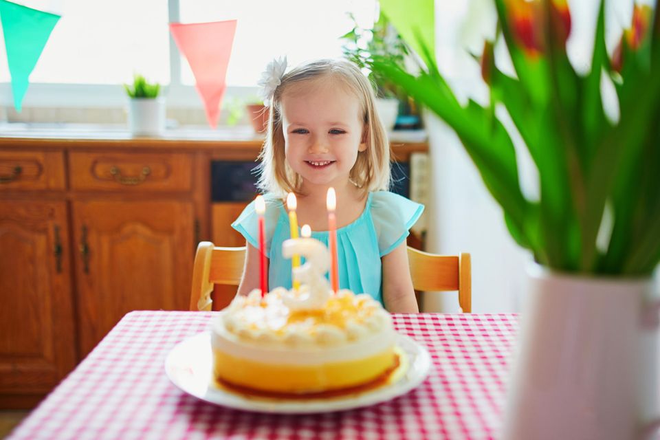Kleines Mädchen sitzt vor einer Geburtstagstorte mit drei Kerzen