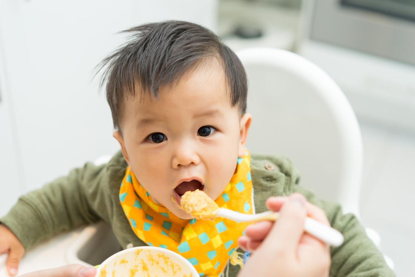 Ein kleiner Junge isst seinen Brei in einem Kinderstuhl