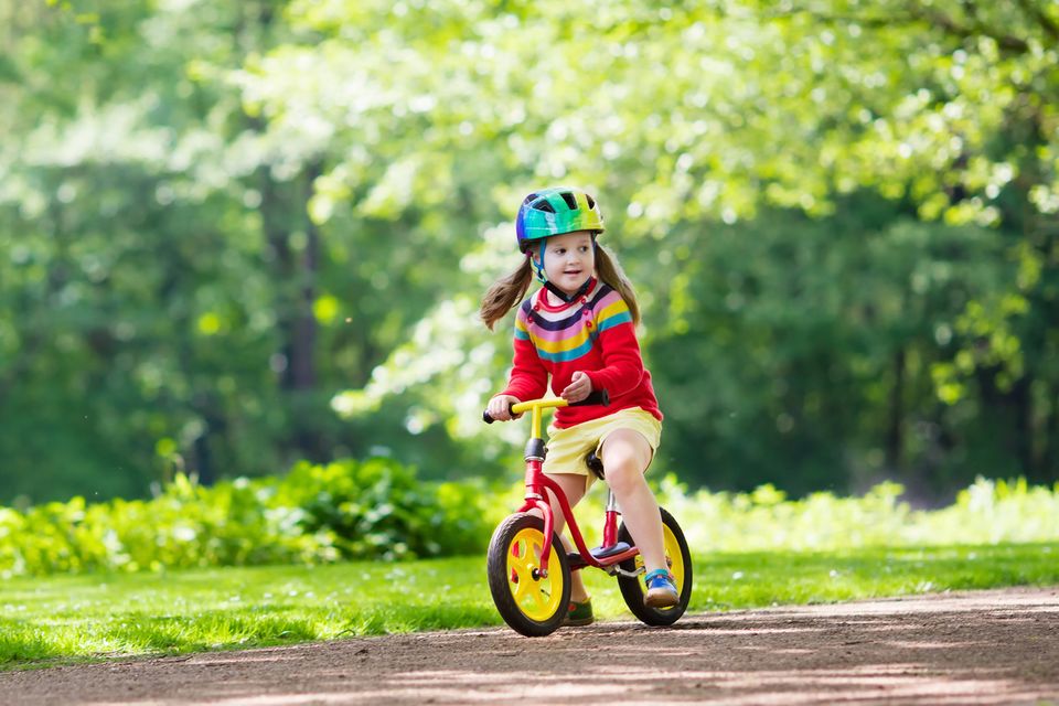 Mädchen ist lächelnd mit Laufrad auf Waldweg unterwegs