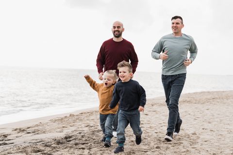 Neue Familienkonstellationen: zwei Väter laufen mit ihren gemeinsamen Kindern am Strand entlang