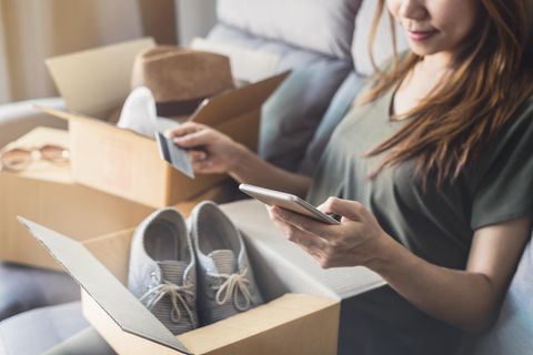 Online Shopping: eine junge Frau sitzt auf dem Sofa, geöffnete Kartons neben ihr und Kreditkarte in der Hand
