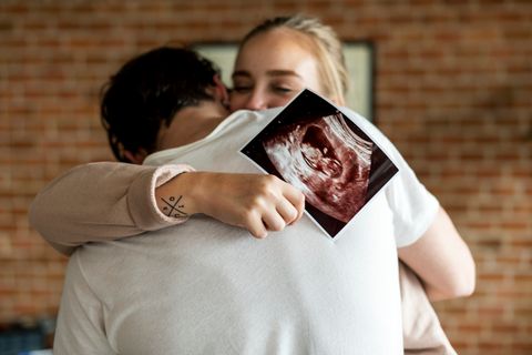 Ein Paar umarmt sich innig, die Frau hält ein Ultraschallbild in ihrer Hand.