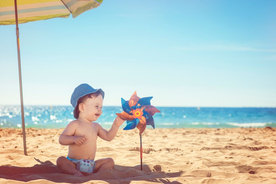 Sonnencreme fürs Baby: Baby sitzt unter Sonnenschirm am Strand