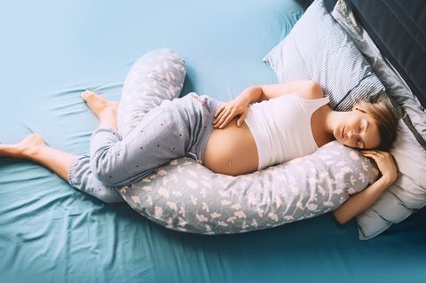 Stillkissen-Test: Schwangere Frau schläft mit langem Stillkissen im Bett.