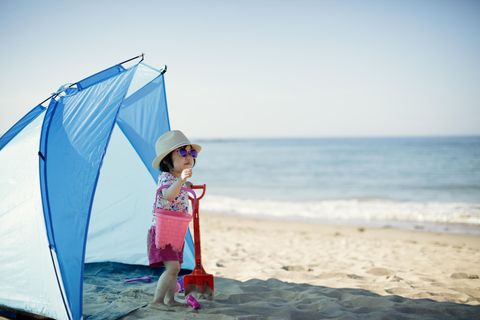 Strandmuschel im Test: Kleines Mädchen spielt im Zeltschatten am sonnigen Strand.