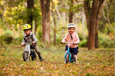 Laufräder im Test: Mädchen und Junge mit Helmen fahren fröhlich mit Laufräder auf einer Waldwiese.