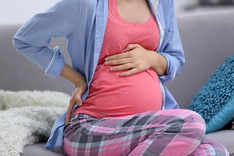 Eine Schwangere hat Übungswehen, sitzt auf der Couch und hält ihren Bauch