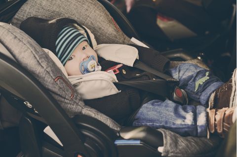 Babyschale im Test: Baby mit Mütze, Jacke und Schnuller sitzt angeschnallt in Babyschale.