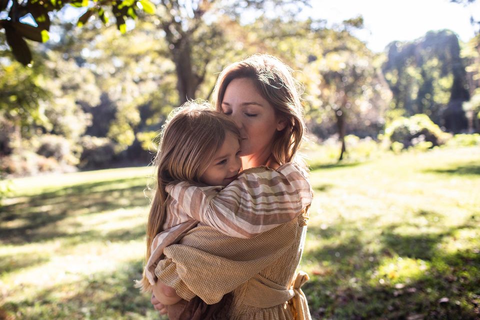 Wertschätzende Erziehung: Mutter umarmt ihre Tochter und gibt ihr einen Kuss auf die Stirn